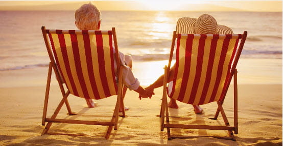A couple holding hands while reclining in chairs watching sunset on the beach