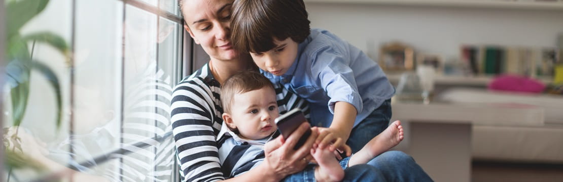 A mother holding two children looking at her phone.